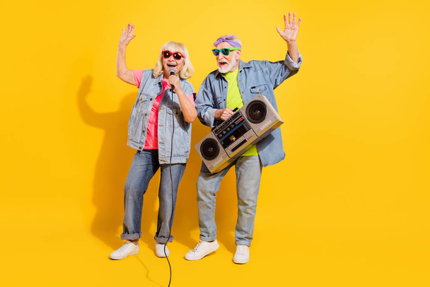 Photo of excited pretty husband wife wear jeans shirts singing listening boombox isolated yellow color background - Zdjęcie, obraz