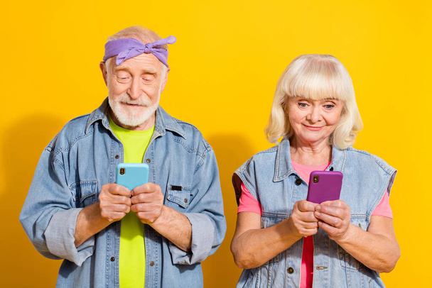 Photo of busy retired husband wife wear jeans clothes typing modern devices isolated yellow color background - Foto, afbeelding