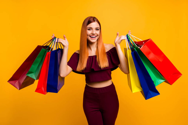Çekici bir kadının fotoğrafı kırmızı elbise giyer yükselen alışveriş alışverişleri izole edilmiş sarı renk arka plan - Fotoğraf, Görsel