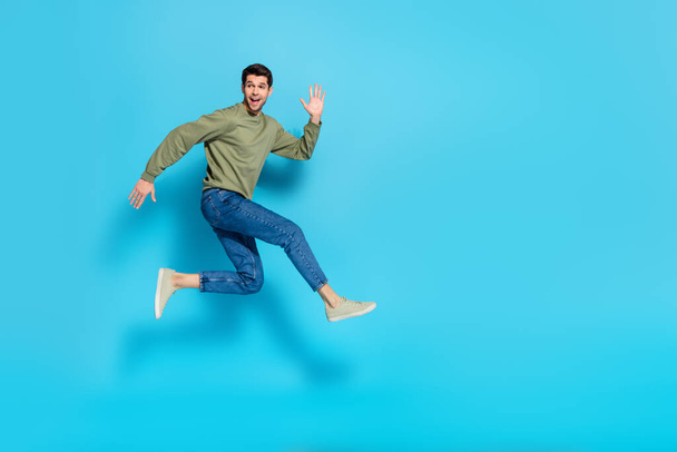 Full body photo of satisfied glad young person enjoy running jump isolated on blue color background - Zdjęcie, obraz