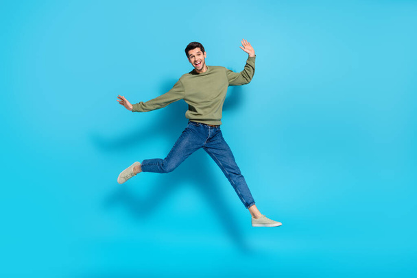 Full length photo of cheerful sporty person good mood jumping isolated on blue color background - Foto, afbeelding
