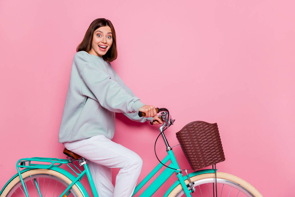 Profile photo of pretty bob hairstyle young lady ride bike wear hoodie isolated on pink background - Zdjęcie, obraz