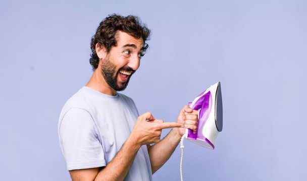young adult hispanic crazy man with a hand iron. housework concept - Φωτογραφία, εικόνα