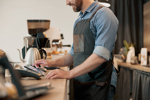 Close up of male barista working in cafeteria and takes order from clients - Photo, image