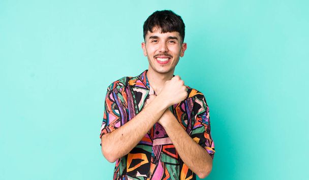 young adult hispanic man smiling cheerfully and celebrating, with fists clenched and arms crossed, feeling happy and positive - Foto, Imagen