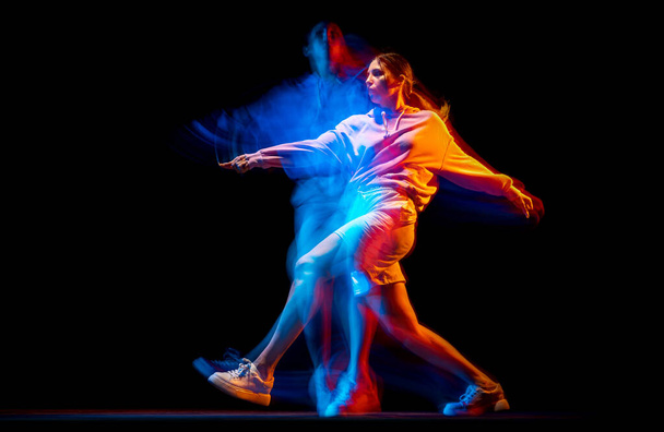 Fiatal nő táncol hip-hop sportos stílusú ruhák elszigetelt sötét háttérrel táncterem vegyes neon fény. Ifjúsági kultúra, hip-hop, mozgás - Fotó, kép