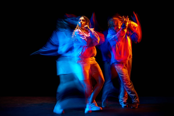 Dynamic portrait of stylish man and girl dancing hip-hop in sportive style clothes on dark background at dance hall in mixed neon light. Youth culture, breakdance, movement - Foto, immagini