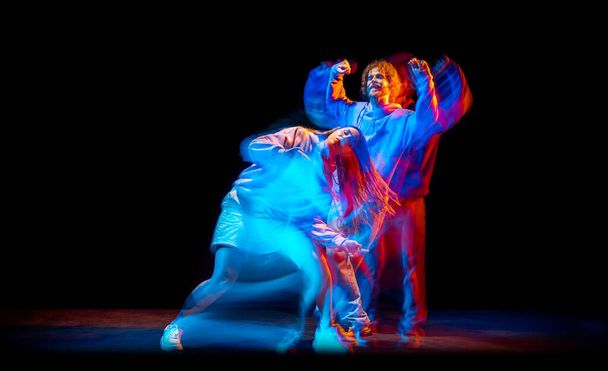 Dans salonundaki karışık neon ışıklı dans salonunda spor tarzı kıyafetlerle hip-hop yapan şık erkek ve kızın dinamik portresi. Gençlik kültürü, break dans, hareket - Fotoğraf, Görsel