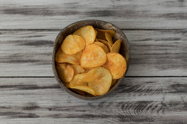 Crispy Potato Chips in a Wicker Bowl on Old Kitchen Table - Fotó, kép