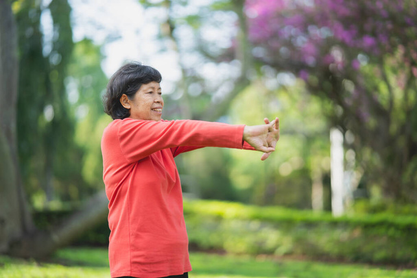 Kıdemli Asyalı kadın vücudu egzersiz yapmadan önce ısınıyor. Bahçede koşmadan önce esneme hareketleri yapan yaşlı kadın, spor koşucusu konsepti.. - Fotoğraf, Görsel