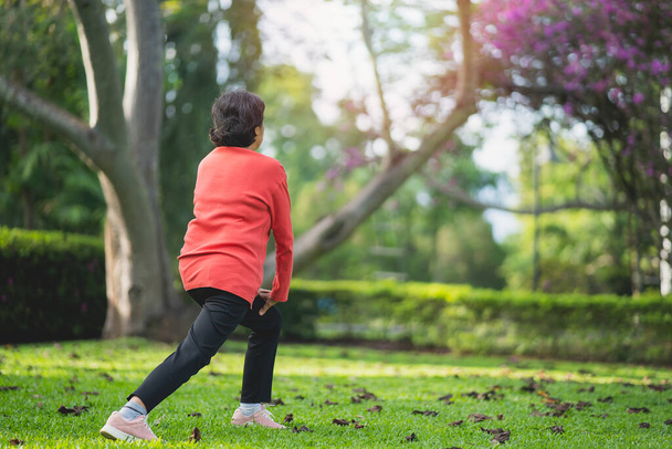 Senior Aziatische vrouw lichaam opwarming voor het sporten. Oude vrouw stretching voor het joggen in de tuin, Sport atleet running concept. - Foto, afbeelding