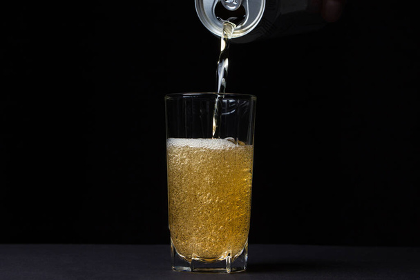 Glass of beer on a black background. Beer is poured into a glass from an aluminum can. Alcoholic drink - Photo, Image