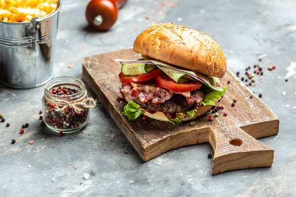 Zelfgemaakte hamburger met sappig vleesmes, groenten, saus frietjes op rustieke grijze achtergrond. fastfood en junk food concept. - Foto, afbeelding