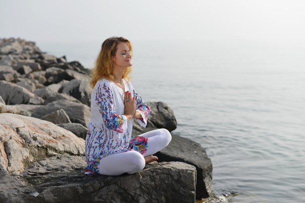 Young woman doing yoga on a rocky ocean shore - Photo, Image