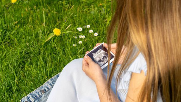 Ultrasound image pregnant baby photo. Woman holding ultrasound pregnancy picture on grass flower background. Pregnancy, medicine, pharmaceutics, health care and people concept - Fotó, kép