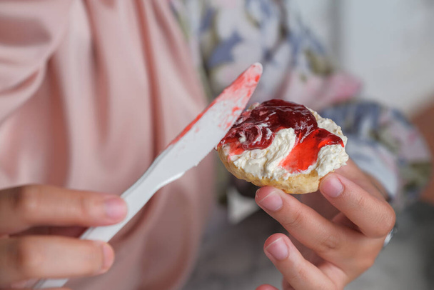 Close up view of a woman holding scone ready to put strawberry jam on scone - Fotó, kép