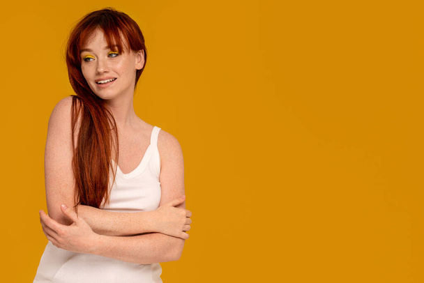 Cute natural redhead woman with delicate smile and yellow makeup posing on colorful studio background, looking away. Casual simple clothes. A lot of copy space - Fotoğraf, Görsel