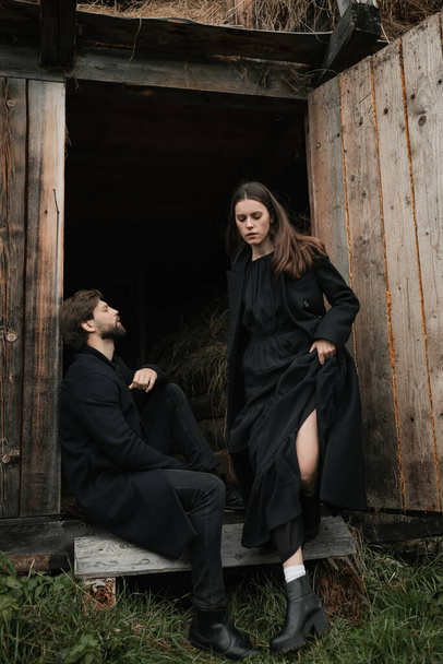 Mladý zamilovaný pár v černých kabátech chodí v dešti po venkově. Podzimní pochmurná nálada. kinematografický obraz - Fotografie, Obrázek