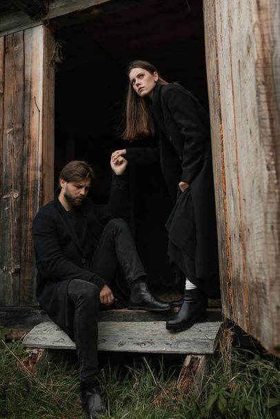 Um jovem casal apaixonado em casacos pretos caminha no campo à chuva. Humor sombrio no Outono. imagem cinematográfica - Foto, Imagem