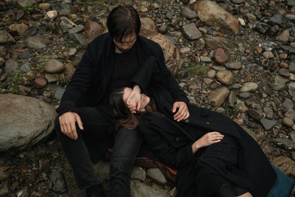 Um jovem casal apaixonado em casacos pretos caminha no campo à chuva. Humor sombrio no Outono. imagem cinematográfica - Foto, Imagem