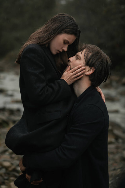 Mladý zamilovaný pár v černých kabátech chodí v dešti po venkově. Podzimní pochmurná nálada. kinematografický obraz - Fotografie, Obrázek