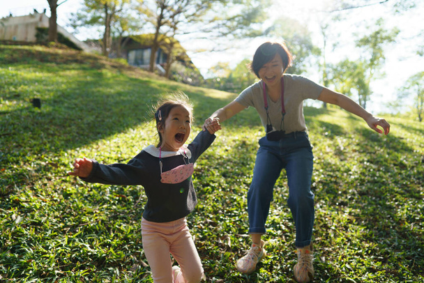 Pohyb záběr šťastné asijské matky a dcery, jak si spolu hrají v parku s náladou teplého ranního slunce. Šťastná rodina. pravá láska a péče. - Fotografie, Obrázek