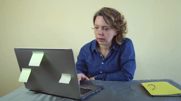 Czterdziestoletnia kobieta w jeansowej koszuli pracuje w laptopie. Kobieta jako wolny strzelec. zwolniony ruch - Materiał filmowy, wideo