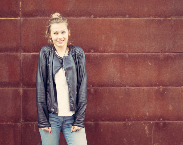 Girl in a black leather jacket posing in a rusty metal wall. Outdoor - Fotó, kép