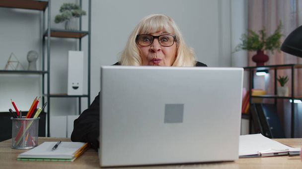 Ältere ältere Geschäftsfrau versteckt sich hinter Laptop-Computer, macht lustiges Gesicht, albert herum - Foto, Bild