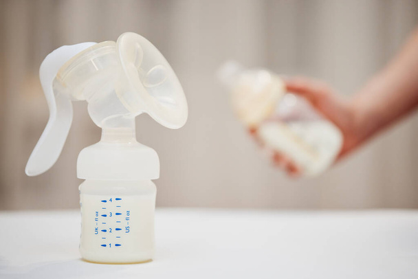 manual breast pump on background of hand with bottle with milk - Foto, imagen