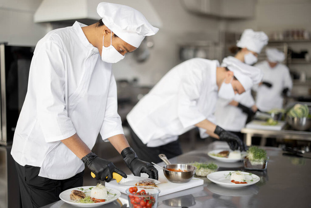 al group of cooks finishing main courses while working together in the kitchen - Photo, Image