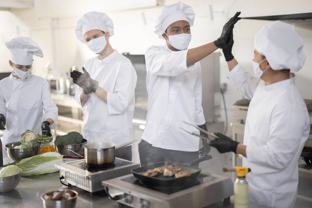 Wielorasowy zespół kucharzy dając pięć rąk do siebie, podczas gotowania w profesjonalnej kuchni - Zdjęcie, obraz