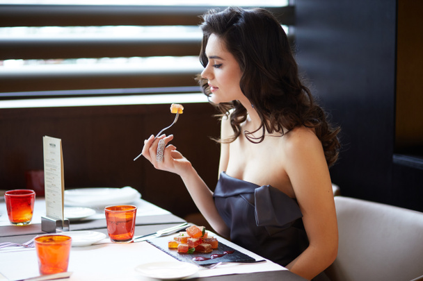 Attractive brunette serves a dessert in the restaurant, wear elegant dress, makeup and hairstyle. Profile portrait. - Foto, afbeelding