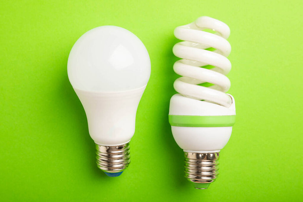 電球がついてる。エネルギー効率の概念です。LEDランプ対白熱灯。緑の背景に構図。経済的で環境に優しい電球の概念を使用する. - 写真・画像