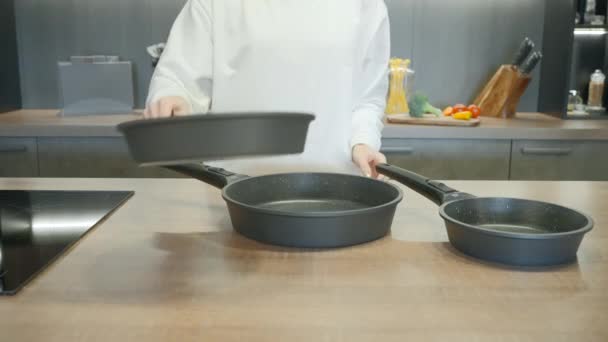Nieuwe set koekenpannen gedemonstreerd door een chef in wit uniform. Actie. Interieur van een moderne keuken. - Video
