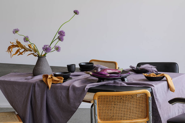 Elegáns asztali beállítás kézműves asztali kerámia edényekkel, padlizsán tányérral, dekoratív fokhagyma vázában. Szezonális zöldségek és virágok az asztalterítőn. Kültéri asztal beállítása a nyári vakáció koncepciójához. - Fotó, kép