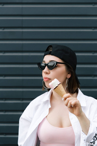 Brunette girl in a cap and shirt eats fun ice cream - Zdjęcie, obraz