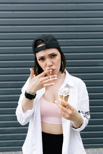 Brunette girl in a cap and shirt eats fun ice cream - Фото, зображення