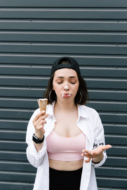Brunette girl in a cap and shirt eats fun ice cream - Photo, Image