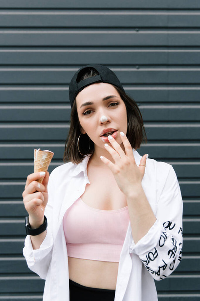 Брюнетка в кепке и рубашке ест веселое мороженое - Фото, изображение