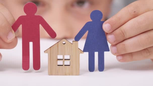 Dos personas de papel se acercan a una casa de madera en manos de un niño - Imágenes, Vídeo