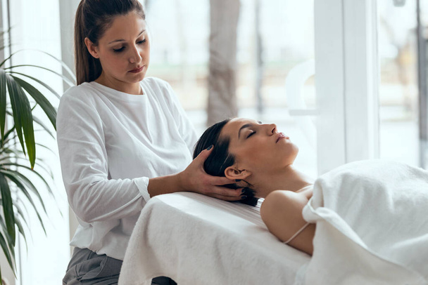 Shot of cosmetologist making relax massage to beautiful woman while lying on a stretcher in the spa center. - Фото, изображение