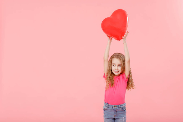 Adorable niña sosteniendo el corazón rojo globo en forma de fondo rosa. Día de la madre, día de San Valentín, amor, sentimiento, concepto familiar - Foto, imagen