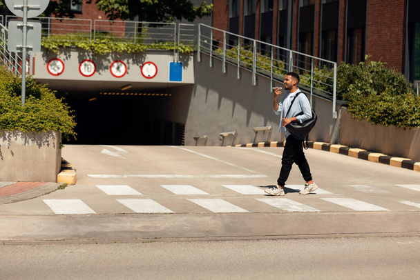 Улыбающийся чёрный мужчина разговаривает по телефону, гуляя по городу - Фото, изображение