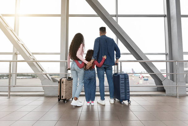Rodina s kufry vyhlíží z okna na letišti při čekání na let - Fotografie, Obrázek
