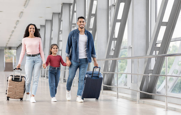 Eindelijk vakantie. Opgewonden glimlachende Arabische familie die handen vasthoudt tijdens het lopen op de luchthaven - Foto, afbeelding