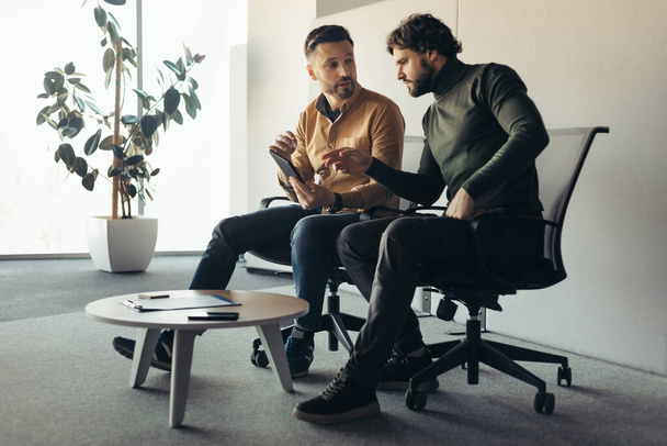 Komoly férfi kollégák kommunikálnak a cég irodájában, táblagépet használnak, megvitatják a közös üzleti projektet - Fotó, kép