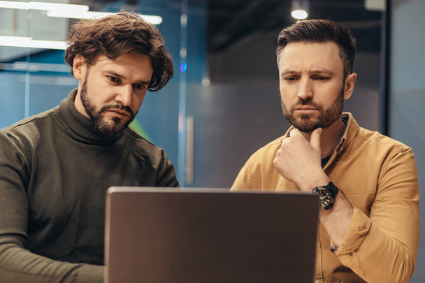 Dos empleados masculinos desarrollando estrategias de negocio, cotrabajando juntos, usando PC portátil en la oficina - Foto, imagen