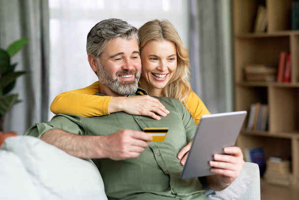 Glückliches Paar mittleren Alters mit digitalem Tablet und Kreditkarte zu Hause - Foto, Bild