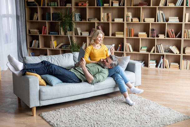 Felice medioevo sposi rilassante con gadget moderni sul divano a casa - Foto, immagini